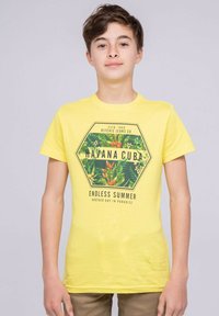 T-shirt en coton jaune avec un imprimé graphique hexagonal comportant des feuilles tropicales et du texte, à manches courtes et avec un col rond.