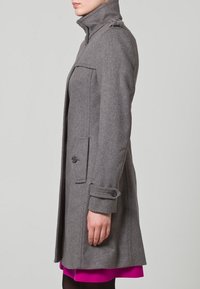 Harmaa villakangastakki, jossa on korkea kaulus, sivutaskut ja napit hihansuiden koristuksena. Suoraleikkainen malli ja sileä pinta.