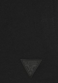 Black knit fabric features a textured surface, with a triangular black rubber logo patch at the lower corner displaying the brand name.