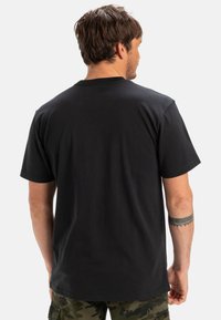 Black cotton t-shirt with a crew neckline and short sleeves. Back view shows a simple design and relaxed fit. Material appears soft.