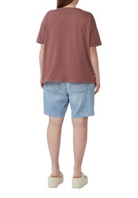 T-shirt en coton marron surdimensionné, associé à un short en denim bleu clair. Doté de manches courtes, d'un col rond et d'un ourlet effiloché.