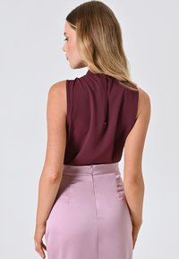 Top senza maniche color bordeaux con dettaglio arricciato al collo, abbinato a una gonna aderente color rosa chiaro con chiusura a zip sul retro.