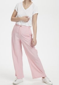 Růžové široké kalhoty s texturovaným povrchem, kombinované s bílým tričkem s výstřihem do V a bílými teniskami, s předním zapínáním na knofl�íky.