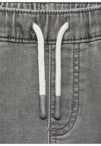 Šedé džíny jogger s páskem na stažení, který má bílé tkané šňůrky, šedé gumové konce a viditelné švy.