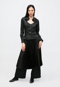 Melna krekla ar pogām un volāniem apkaklī, kopā ar plisētu melnu svārku un plaša silueta melnām biksēm. Izskatam pievienotas šauras, spīdīgas melnas kurpes.