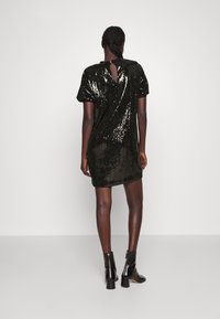 Svart paljettklänning med korta ärmar, detaljer med nyckelhål i ryggen och en figurnära passform, i kombination med svarta ankelskor. Slät, glänsande textur.