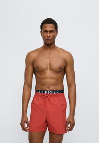 Κόκκινα μαγιό σορτς με ελαστική μέση που διαθέτει μπλε λωρίδα με λογότυπο και μπροστινό κορδόνι, λεία υφή, σχεδιασμός μέχρι το γόνατο.