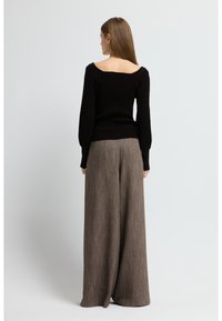 Svart ribbad tröja med bred halsringning, kombinerad med lösa, bruna texturerade byxor. Outfitten har en avslappnad passform.