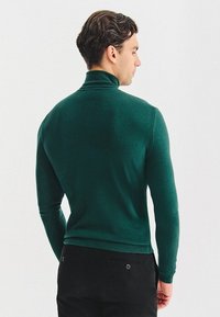 Zielony sweter typu golf wykonanego z miękkiego materiału. Dopasowany krój, długie rękawy i ściągacze. Gładka tekstura bez widocznych wzorów czy akcentów.