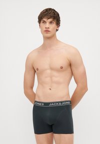 Črne bokserice z prilagodljivim pasom, na katerem je v beli barvi napis "JACK & JONES". Tkanina se zdi mehka in ima gladko teksturo.