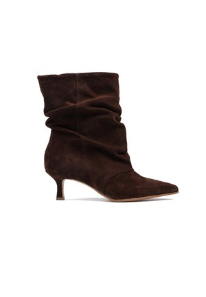 Ciemnobrązowy zamszowy, luźny botek do połowy łydki z zaostrzonym noskiem i niskim obcasem typu kitten na białym tle.