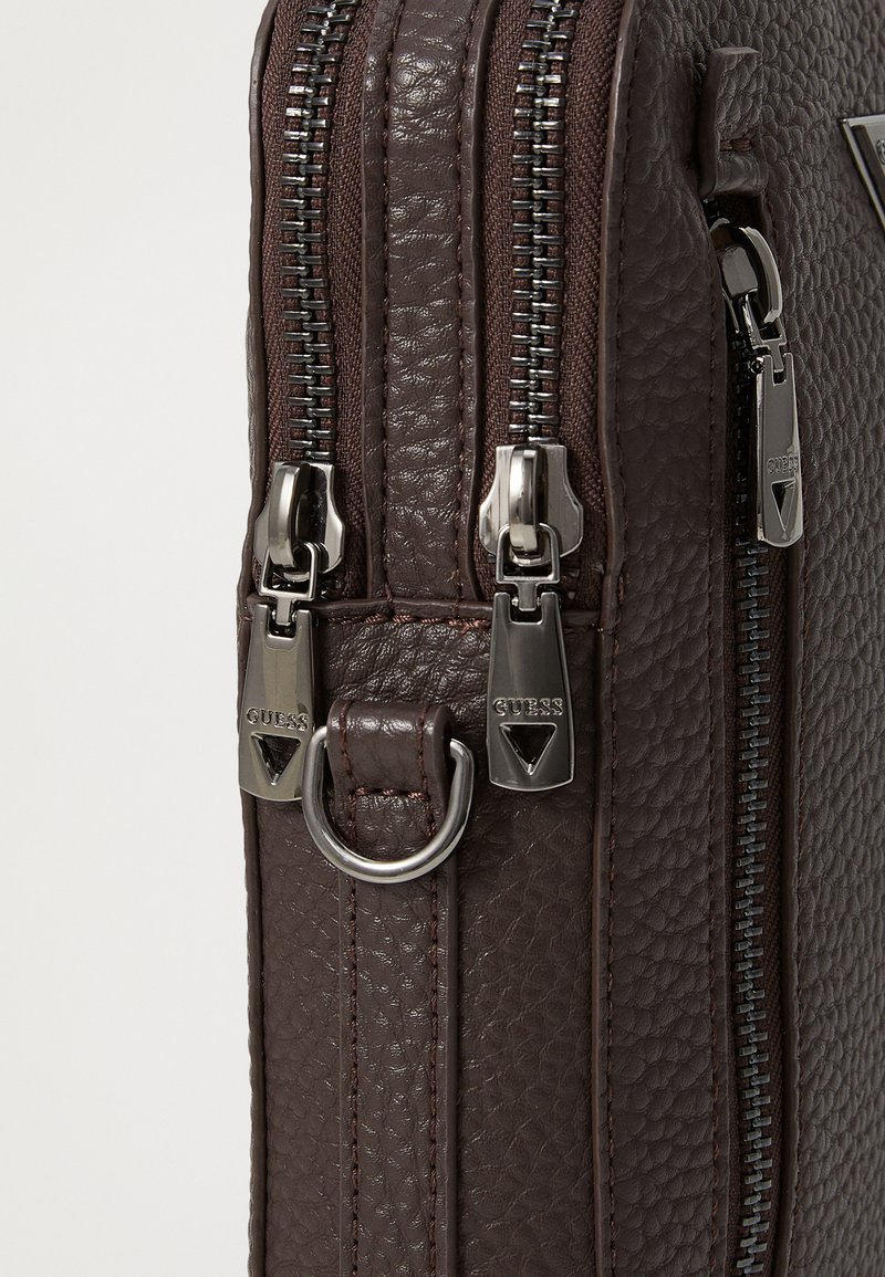 Bolso de cuero texturizado marrón oscuro con dos cremalleras y herrajes plateados. Presenta un anillo de metal y acentos de marca como detalle.