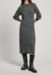Robe grise en tricot avec un motif en losanges, décolleté ras du cou et manches bouffantes. Associée à de hautes bottes en cuir noires et un tissu texturé.