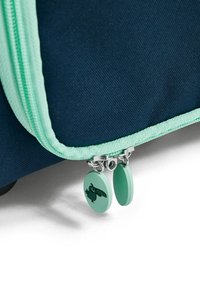 Marinblå tygväska med mintgrön dragkedja och dragkedjesnon. Dragkedjesnon har en cirkelform med ett kaninmönster. Texturerad materialdetalj synlig.