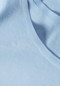 Țesătură de culoare albastru deschis, cu o textură moale, având un decolteu neted și o cădere casuală, relaxată. Fără modele sau elemente metalice vizibile.