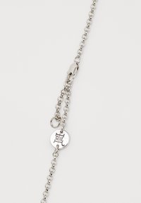 Silver chain bracelet featuring interconnected links, a lobster clasp, and a circular tag with engraved design. Smooth texture, sleek finish.