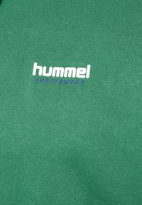 Grønt stof med hvide "hummel" og blå "SPORTSWEAR" logoer trykt i midten.