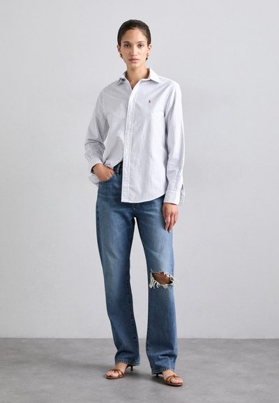 Chemise à rayures blanches et bleues, coupe décontractée, assortie à un jean bleu clair déchiré et des sandales brunes à lanières. Tenue simple et décontractée.