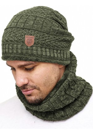 Knit beanie and neck warmer set in olive green, featuring ribbed texture and a leather logo patch on the hat. Soft, cozy fabric.