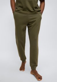 Φόρμες σε ελαιί πράσινο με στενή σχεδίαση, ελαστικές μανσέτες, πλαϊνές τσέπες και μαλακό, υφασμάτινο ύφος.