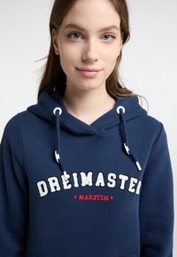 Felpa con cappuccio blu navy dal texture morbido, con ricamo bianco e rosso con la scritta "DREIMASTER MARITIM" sul davanti.