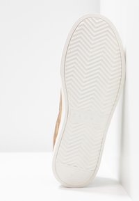 Baskets couleur camel avec une tige en daim texturé et une semelle en caoutchouc blanche présentant un motif en chevrons. Logo embossé sur le côté. Taille 37.