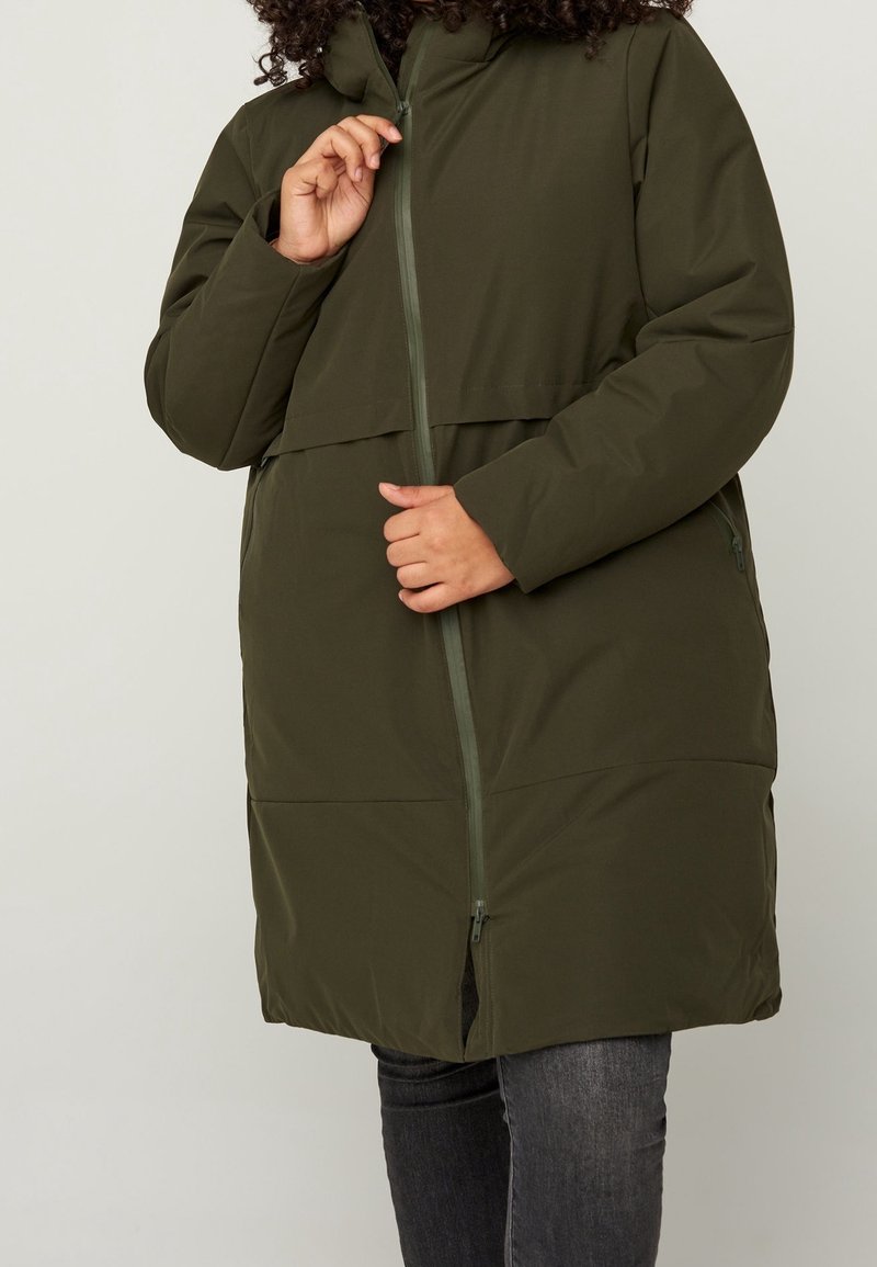 Kurtka puchowa o długości do połowy ciała w kolorze oliwkowej zieleni, zapinana na zamek błyskawiczny, z kapturem i dwoma bocznymi kieszeniami; gładka tekstura z lekko pikowanym wzorem.