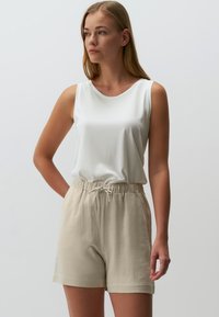 Witte mouwloze top met een ronde halslijn, gecombineerd met lichtbeige linnen shorts met een elastische tailleband en trekkoord.