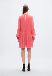 Vestito rosa a maniche lunghe con schiena a goccia, vita arricciata e gonna fluida. Il materiale sembra leggero e testurizzato.