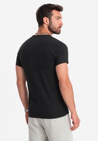 Sort bomulds T-shirt med korte ærmer og rund hals, glat tekstur, tætsiddende design, vist fra ryggen med grå shorts.