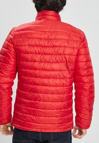 Chaqueta acolchada roja con cuello alto y costuras horizontales. Tejido suave y brillante. Mangas largas y forma ceñida.