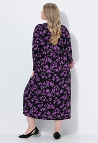 Maxi dress nero a fiori con stampa di fiori viola, maniche lunghe e silhouette fluida; abbinato a ballerine nere.
