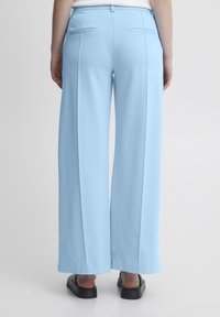 Gaiši zili plata kāju bikses, izgatavotas no mīksta auduma, ar divām aizmugures kabatām un brīvu piegriezumu. Gluda tekstūra, ar taisnu griezumu apakšmalā.