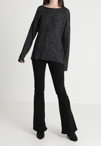 Černý svetr s dlouhým rukávem a volným střihem, vyrobený z texturované pleteniny. Kombinovaný s rozšířenými černými kalhotami a botami na podpatku.