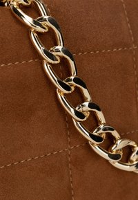 Materiale in suede marrone con una texture trapuntata, dotato di una tracolla in catena dorata lucida con anelli interconnessi e lisci.