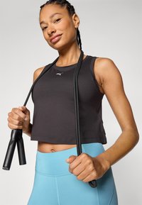 Black cropped athletic tank top with a small white logo, paired with light blue high-waisted leggings, holding a black jump rope.