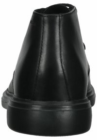 Bottines en cuir noir avec une texture lisse, bout rond et surpiqûres renforcées à l'arrière. Elles présentent une semelle en caoutchouc basse.