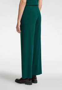 Pantalones anchos verdes con una cintura elástica, hechos de una tela suave, con una textura sutil. Botas negras gruesas completan el conjunto.