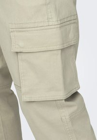 Beige cargobroek van gestructureerde stof, met grote zijzakken, verstevigde stiksels en een recht model.