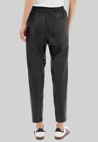 Pantalons de jogging en simili cuir noir avec une taille élastique, des jambes fuselées et une poche arrière, accompagnés de chaussures blanches et noires.