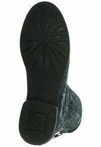 Botte en tissu bleu avec motif floral, semelle texturée et fond en caoutchouc noir présentant un design de bande de roulement en forme de flèche et des marques.
