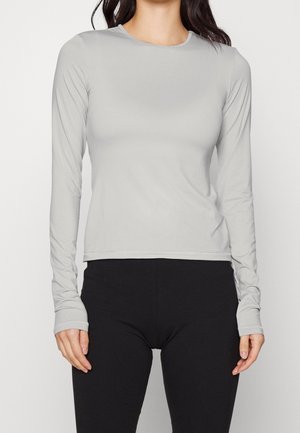 Femme portant un haut gris clair ajusté à manches longues avec des trous pour le pouce et des leggings noirs, montrée du cou aux hanches.