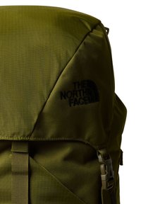 Mochila verde oliva fabricada con nylon texturizado, con un diseño triangular, logo negro y correas ajustables.
