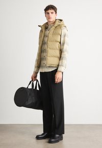 Giacca imbottita beige con cappuccio sopra una maglietta a strisce, pantaloni neri a gamba larga e stivali neri alla caviglia. Tiene una borsa rotonda nera.