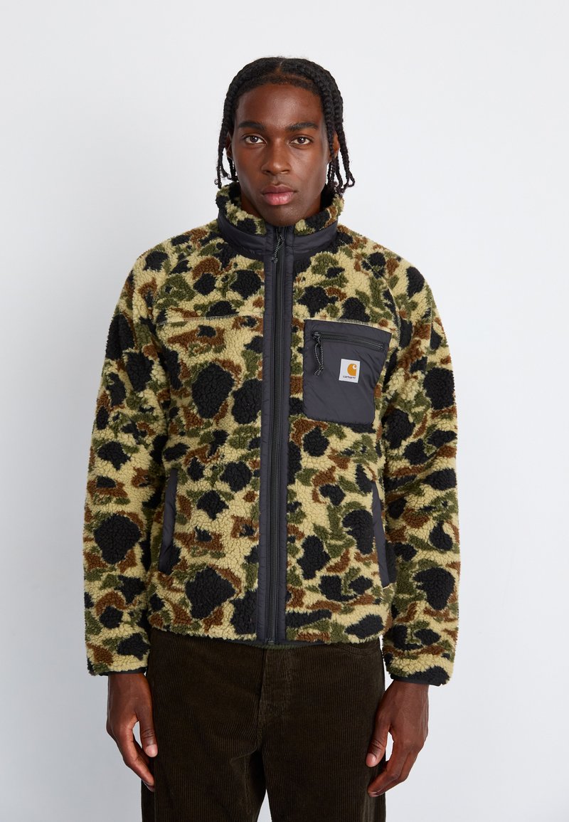 Veste en polaire avec un motif camouflage vert et marron, dotée d'une fermeture éclair noire et d'une poche avec logo. Texture douce et coupe décontractée.