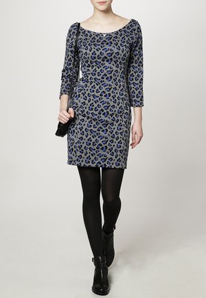 Robe à imprimé léopard gris avec des manches trois-quarts, des accents bleus et une silhouette ajustée ; portée avec des collants noirs et des bottines.