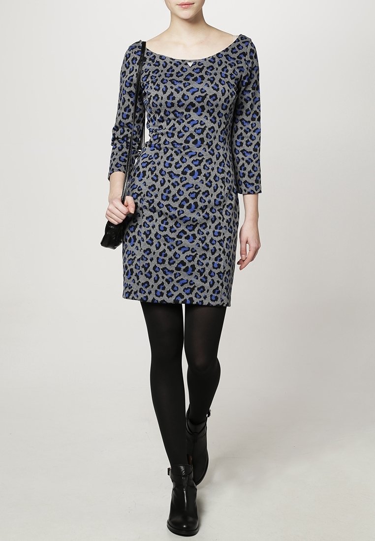 Robe à imprimé léopard gris avec des manches trois-quarts, des accents bleus et une silhouette ajustée ; portée avec des collants noirs et des bottines.