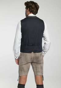 Marineblauer Weste aus strukturiertem Stoff, mit Befestigungsband auf der Rückseite, kombiniert mit grauen Shorts mit blauen Akzenten und einer Schlaufen-Detail.