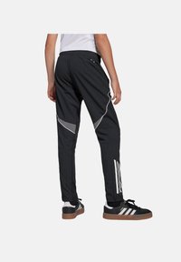 Schwarze Sporthose mit schmaler Passform, ausgestattet mit reflektierenden Akzenten und weißen Seitestreifen. Hergestellt aus leichtem, strukturiertem Material.