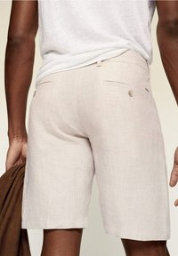 Beige Leinen-Shorts mit geradem Schnitt, ausgestattet mit einem kleinen Knopfverschluss an den Gesäßtaschen und einer glatten, strukturierten Stoffoberfläche.